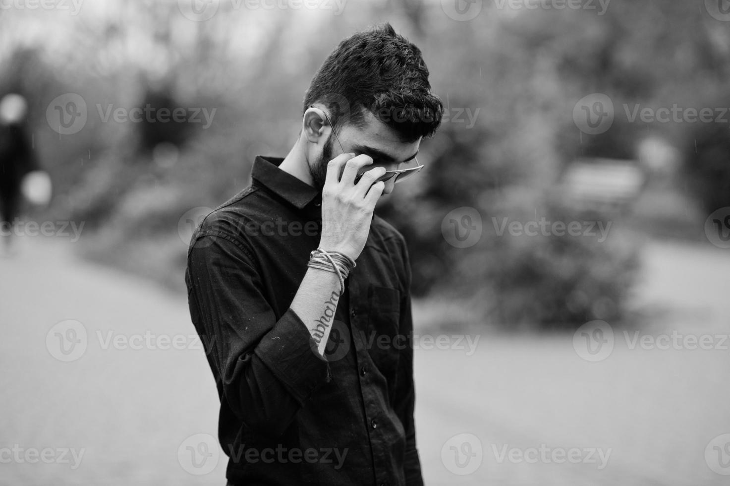 uomo alla moda indiano in camicia nera e occhiali da sole poste all'aperto. foto in bianco e nero.