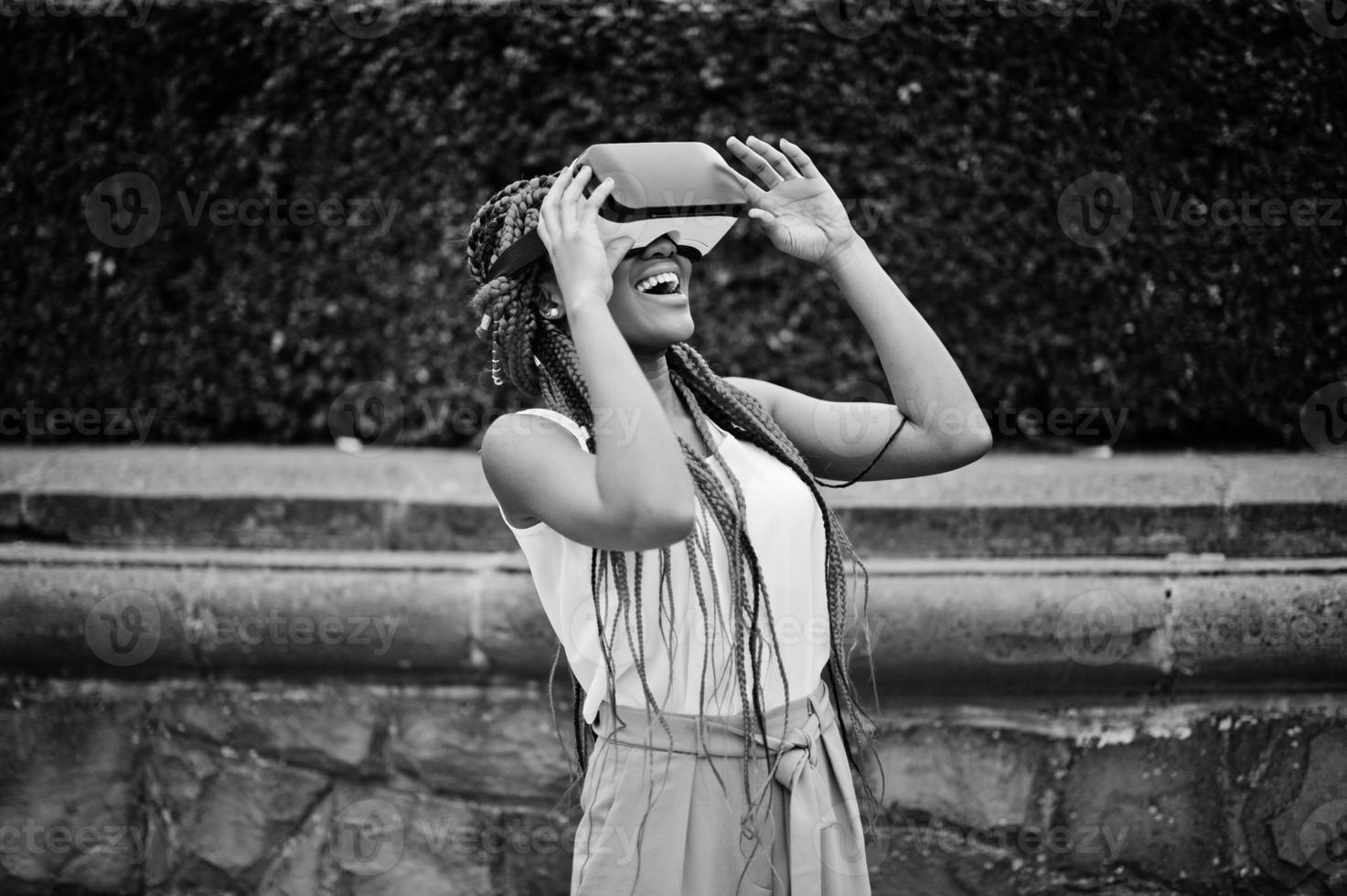 donna alla moda di affari dell'afroamericano a pantaloni rosa e teme rossi con i vetri di realtà virtuale all'aperto. foto