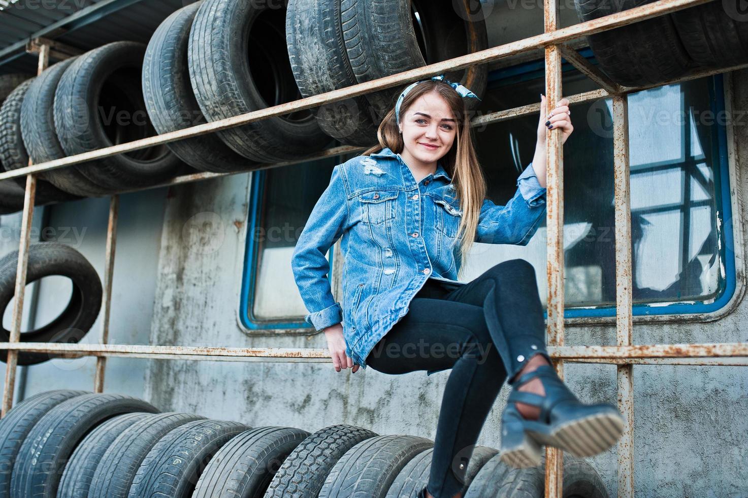 giovane ragazza hipster in giacca di jeans e sciarpa per la testa nella zona di montaggio dei pneumatici. foto