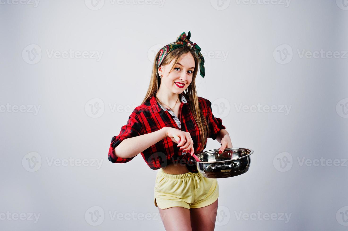 giovane casalinga divertente in camicia a scacchi e pantaloncini gialli pin up style con padella isolata su sfondo bianco. foto