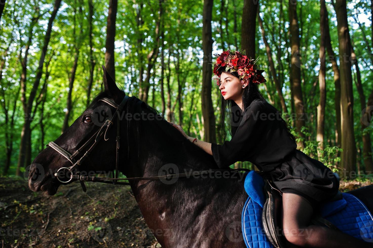 ragazza mistica in ghirlanda indossata in nero a cavallo in legno. foto