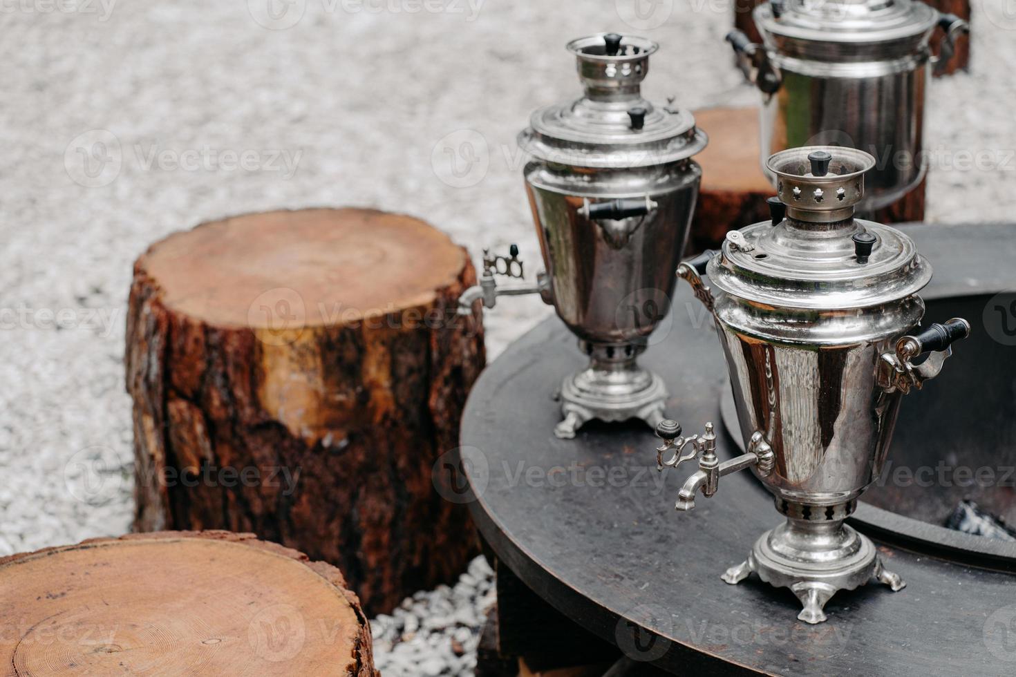 concetto tradizionale di bere il tè. tre antichi samovar di rame in metallo all'aperto vicino a ceppi di legno. stile rustico. foto