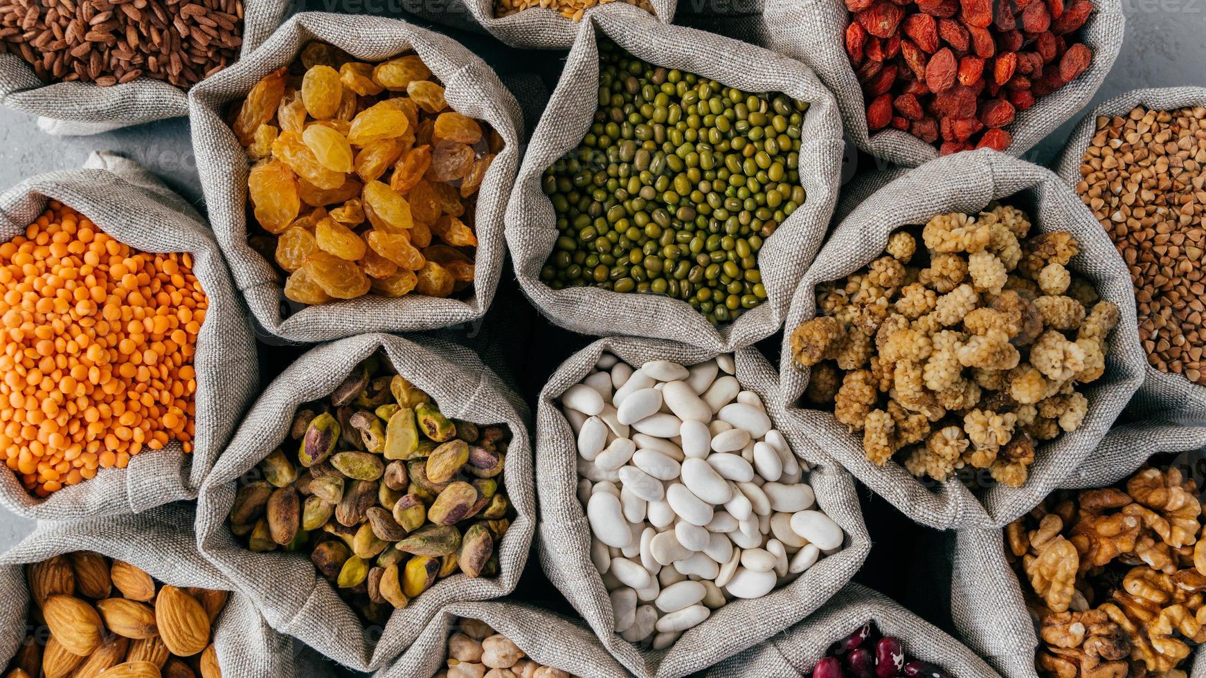 cereali sani e frutta secca. primo piano vista dall'alto di piccole borse con semi di legumi secchi. diversi tipi di fagioli. grani naturali. foto