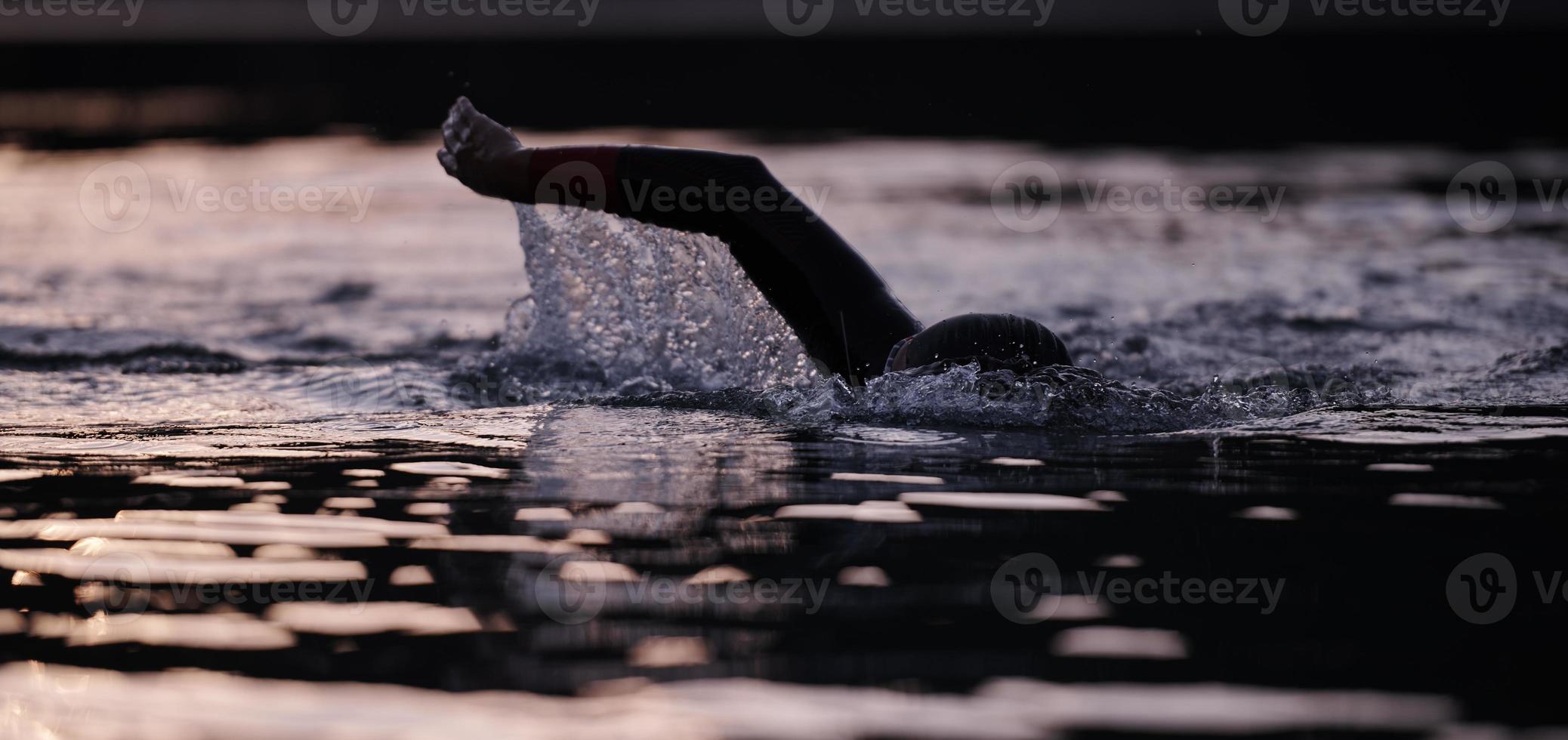 atleta di triathlon che nuota sul lago all'alba indossando la muta foto