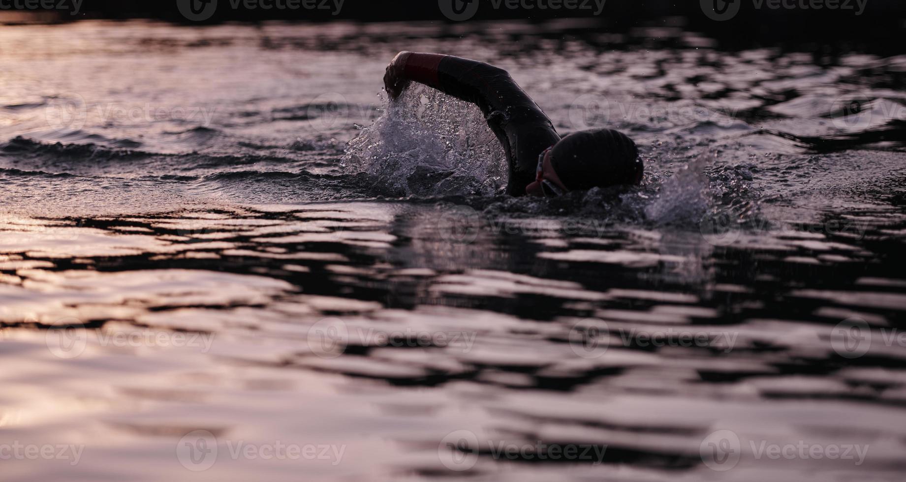 atleta di triathlon che nuota sul lago all'alba indossando la muta foto