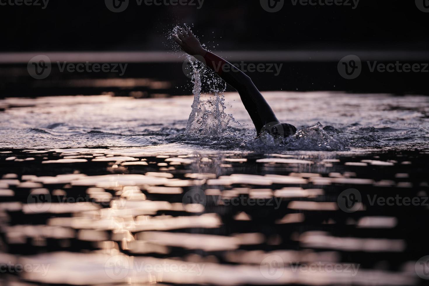 atleta di triathlon che nuota sul lago all'alba indossando la muta foto