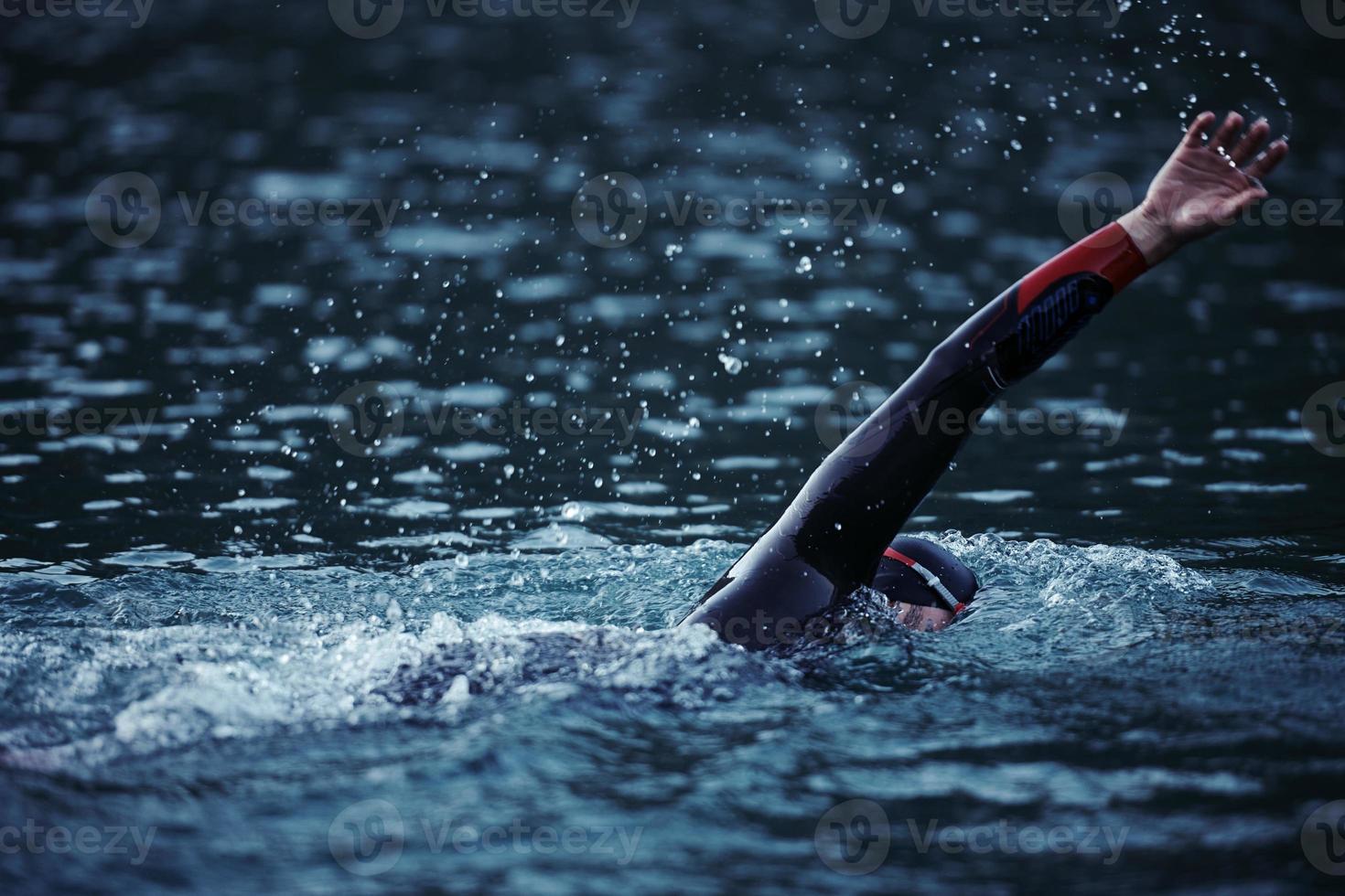 atleta di triathlon che nuota sul lago all'alba indossando la muta foto