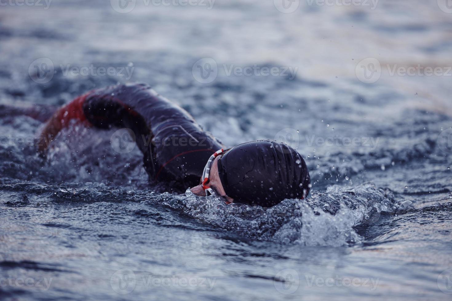 atleta di triathlon che nuota sul lago all'alba indossando la muta foto