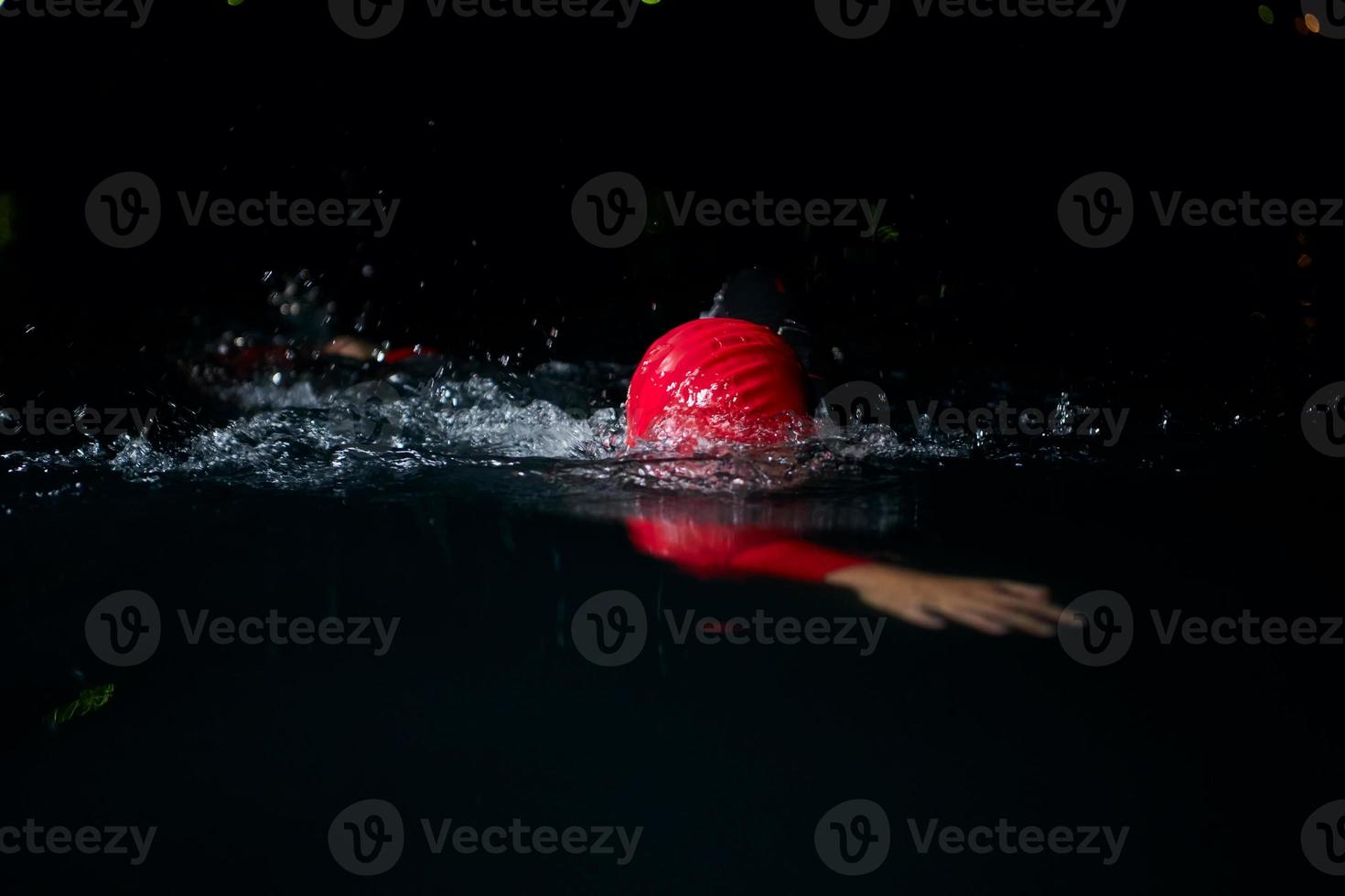 atleta di triathlon che nuota nella notte buia che indossa la muta foto