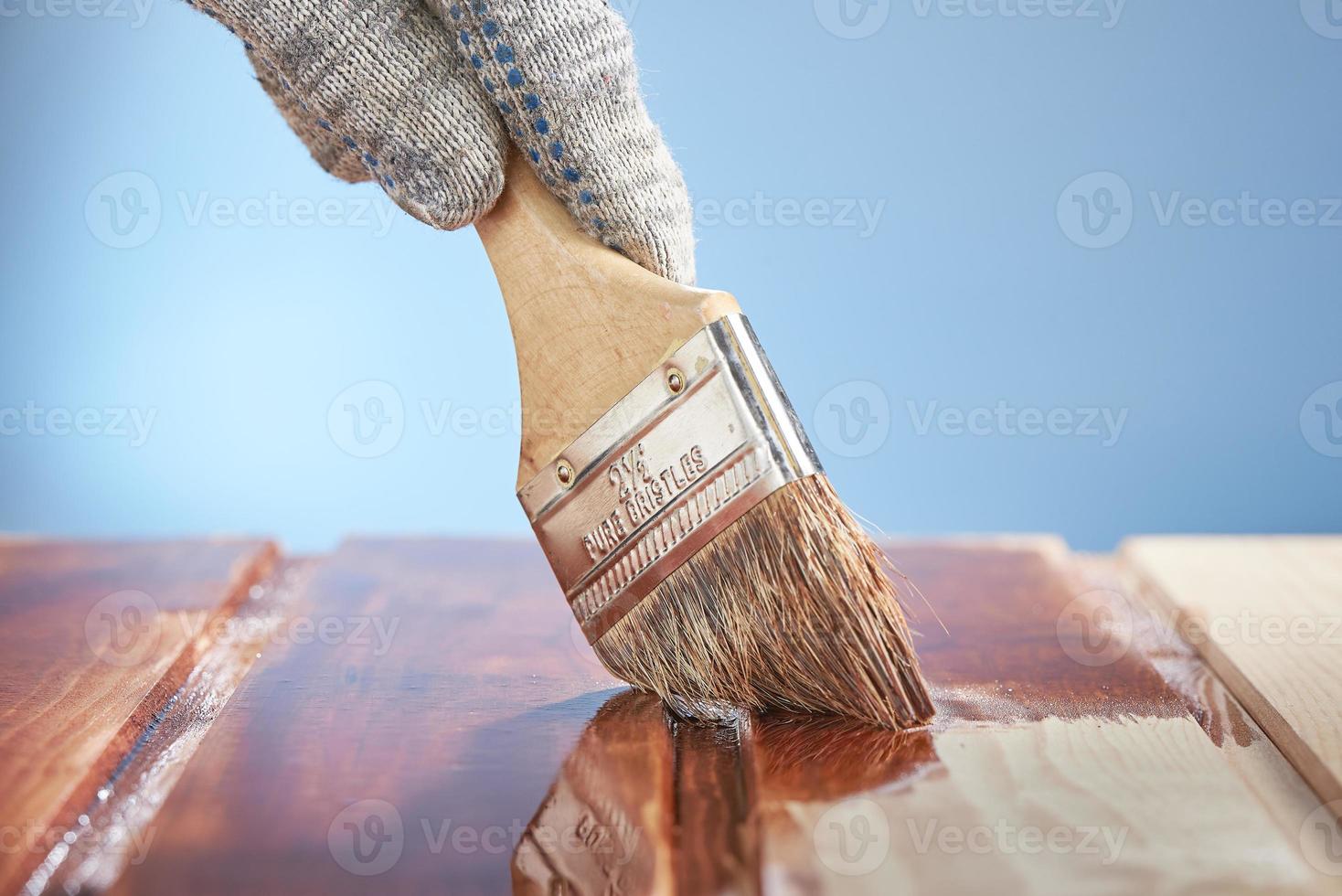 mano d'uomo con un pennello che dipinge la superficie di legno su sfondo blu. foto