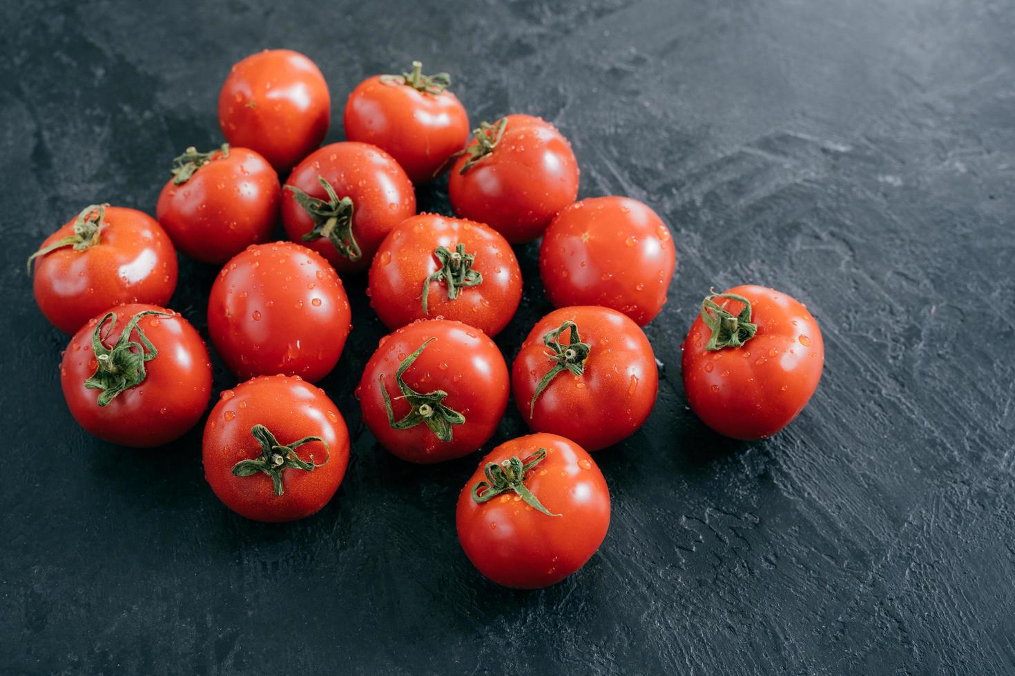 verdure biologiche e concetto di alimentazione sana. pomodori rossi raccolti con gocce d'acqua, sfondo nero. primo piano trama. mercato all'aperto foto