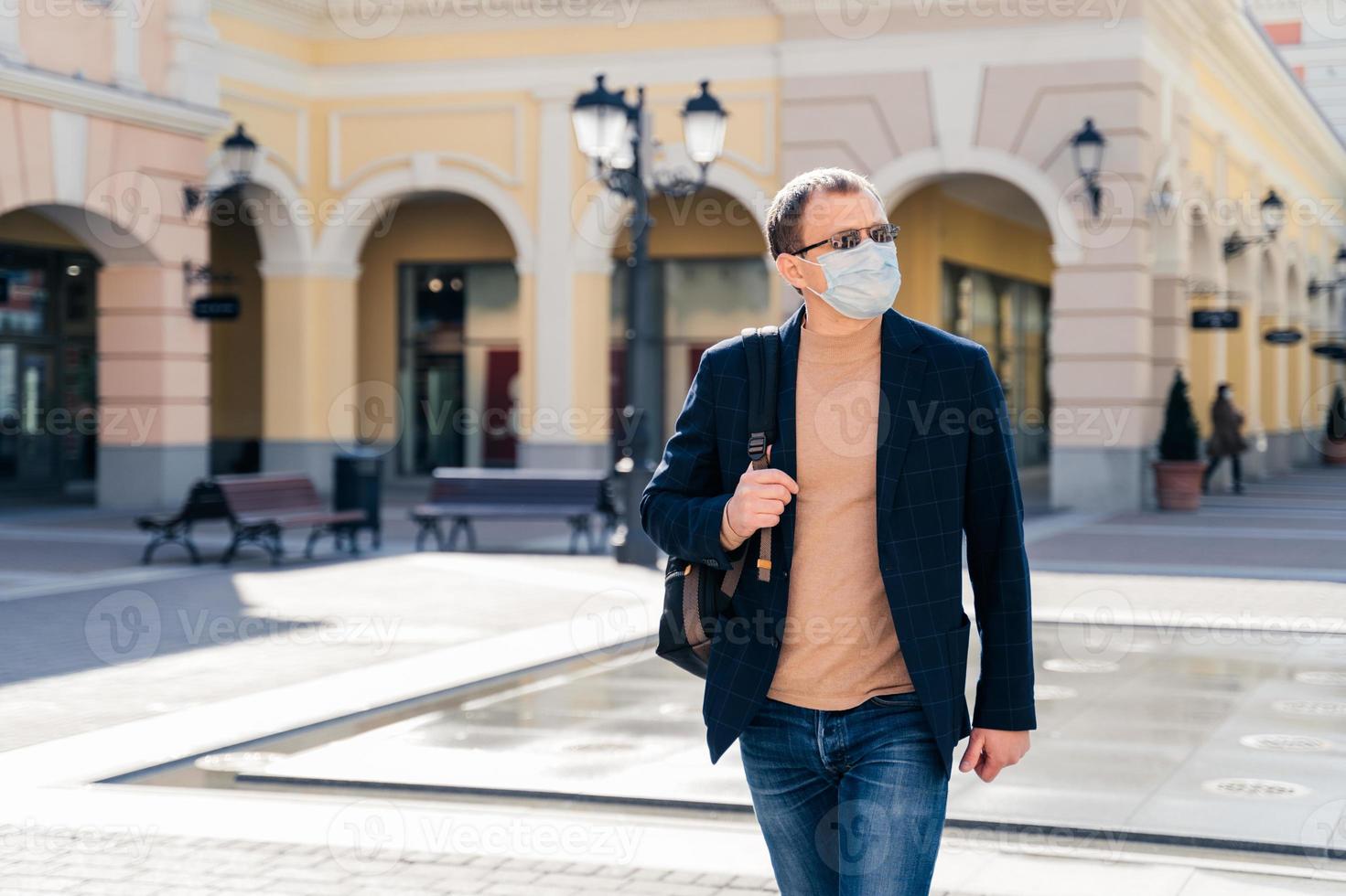scatto all'aperto di un uomo serio cammina sulla stazione con lo zaino, concentrato da parte, indossa una maschera medica per prevenire il virus, aspetta l'autobus o il treno, si preoccupa della salute. concetto di pandemia di coronavirus. foto