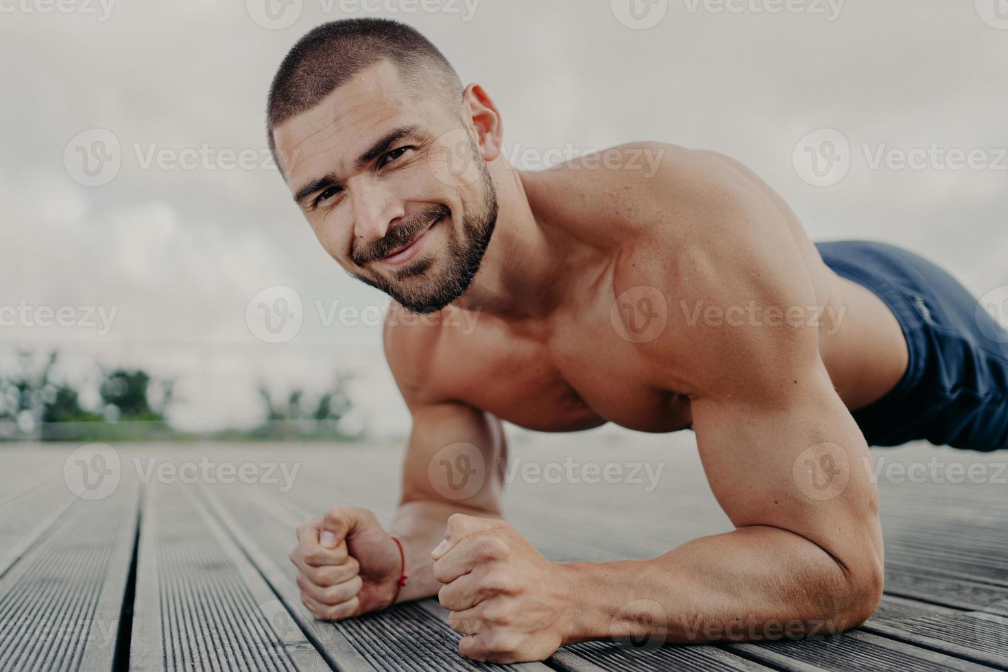 bel sportivo barbuto sta in tavola e fa sport all'aperto, si allena regolarmente e lavora sui muscoli, mostra i suoi bicipiti, cerca di fare del suo meglio. l'uomo fa esercizio di push up. foto