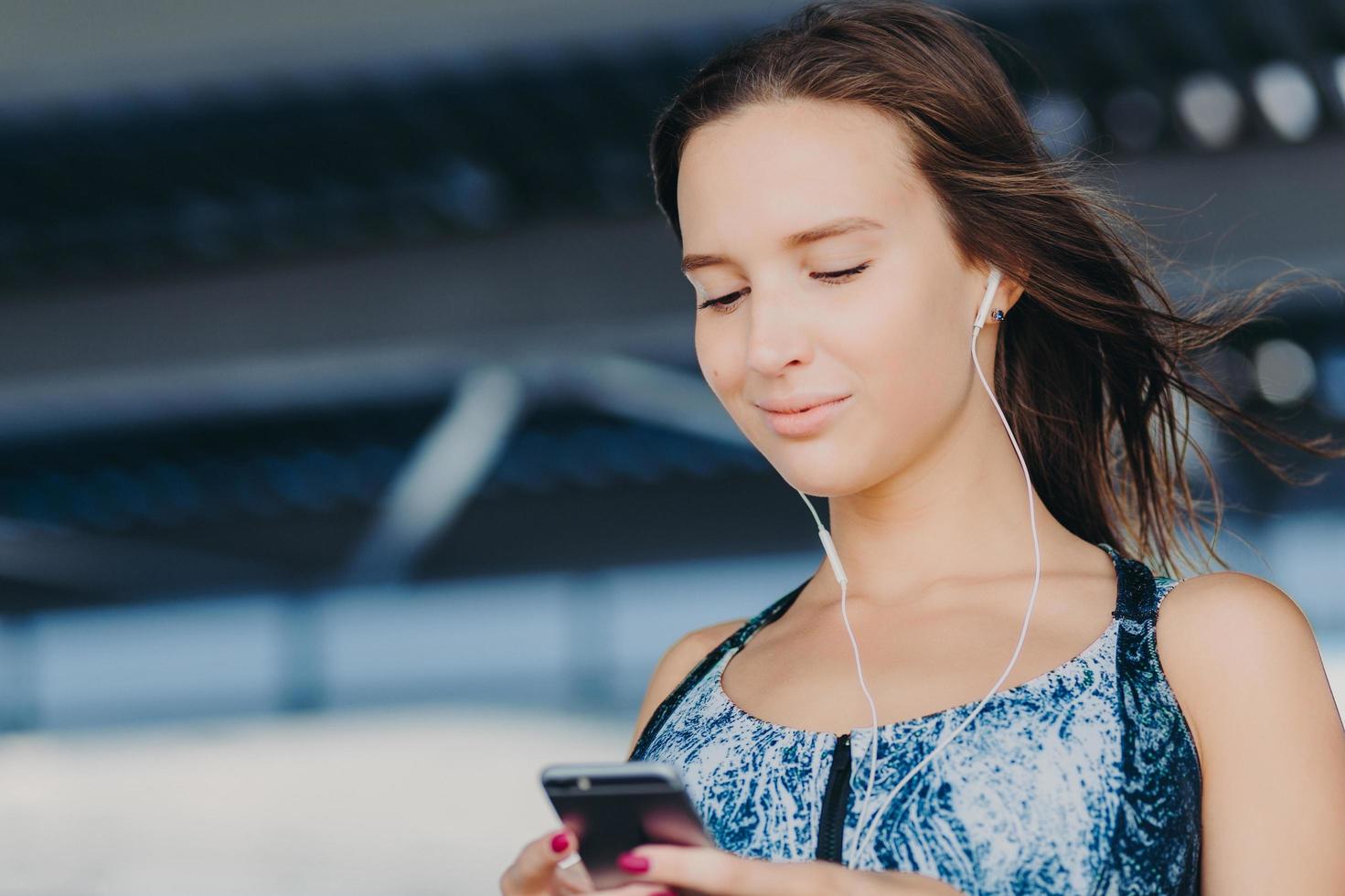 il ritratto ravvicinato di una giovane donna attraente tiene uno smartphone, invia un feedback di testo, controlla la casella di posta elettronica, ascolta la musica nel lettore, scarica le notizie, è connesso a Internet wireless. persone, concetto di svago foto