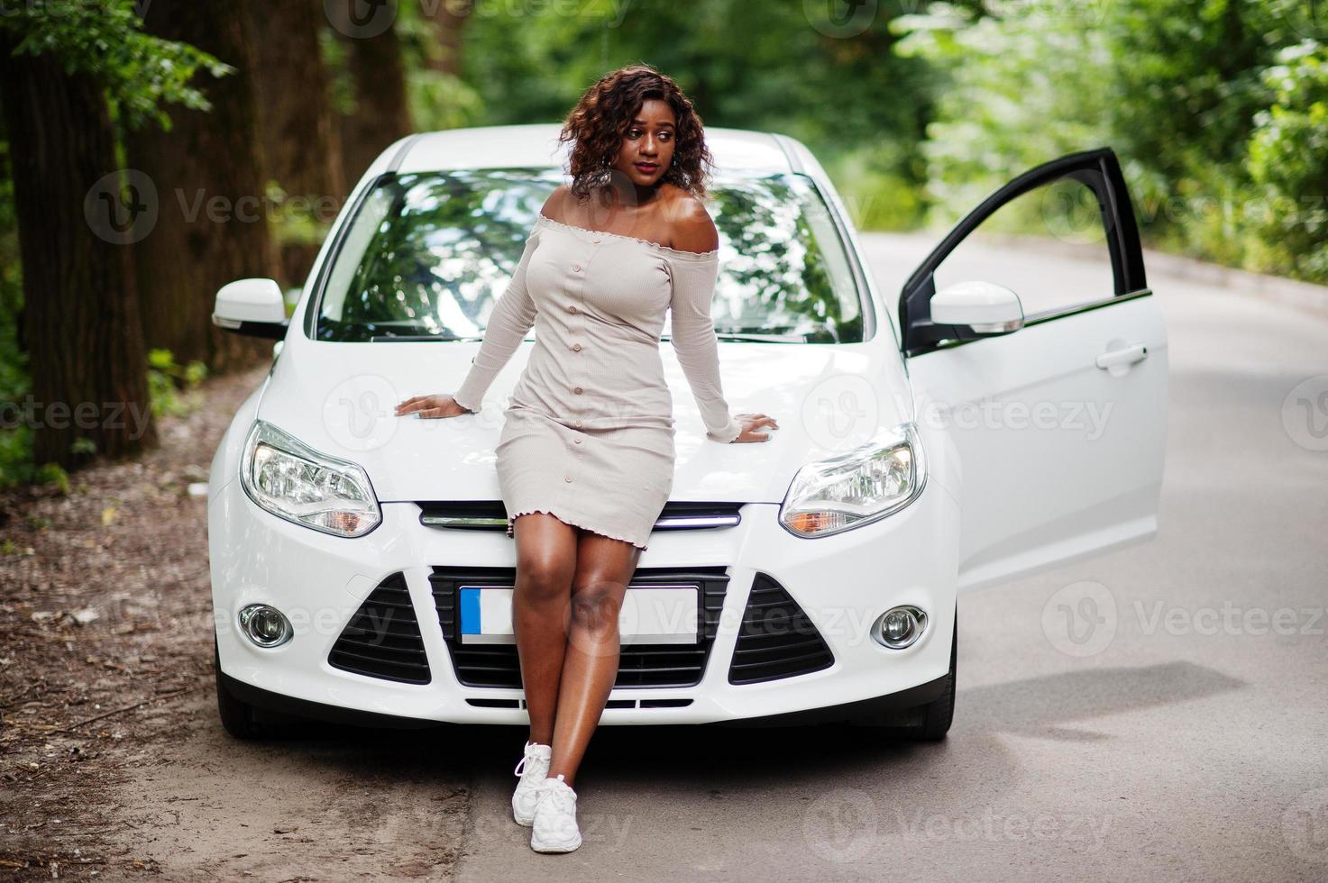 donna afroamericana posata contro un'auto bianca in strada forestale. foto