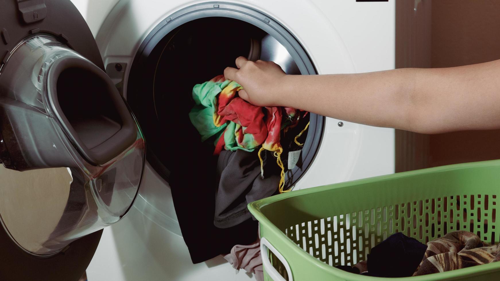 primo piano della mano di una donna che mette i vestiti sporchi nella lavatrice foto