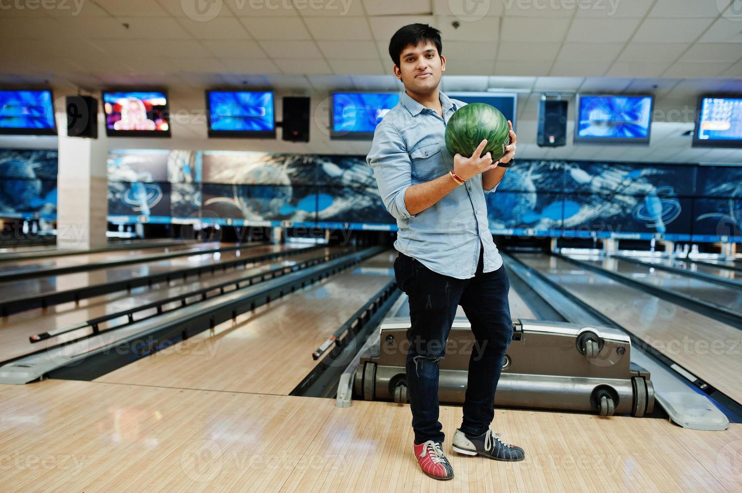 uomo asiatico alla moda in camicia di jeans in piedi alla pista da bowling con palla a portata di mano. foto