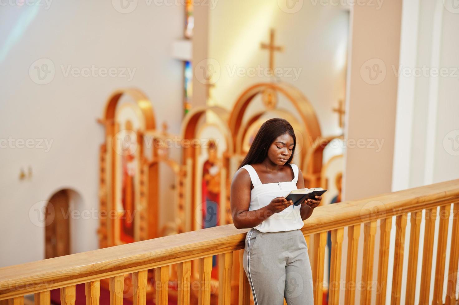 donna afroamericana che prega nella chiesa. i credenti meditano nella cattedrale e nel tempo spirituale della preghiera. ragazza afro con la Sacra Bibbia a portata di mano. foto