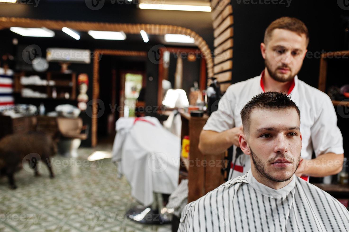 giovane uomo barbuto che si fa tagliare i capelli dal parrucchiere mentre è seduto su una sedia al barbiere. anima da barbiere. foto