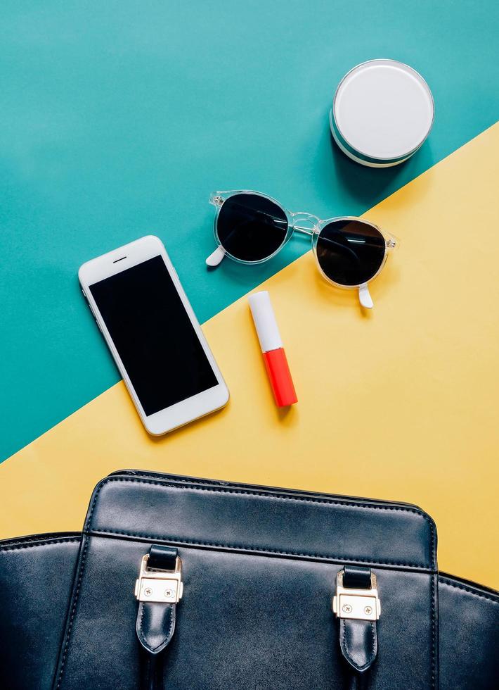 borsa da donna piatta in pelle nera aperta con cosmetici, accessori e smartphone su sfondo colorato foto