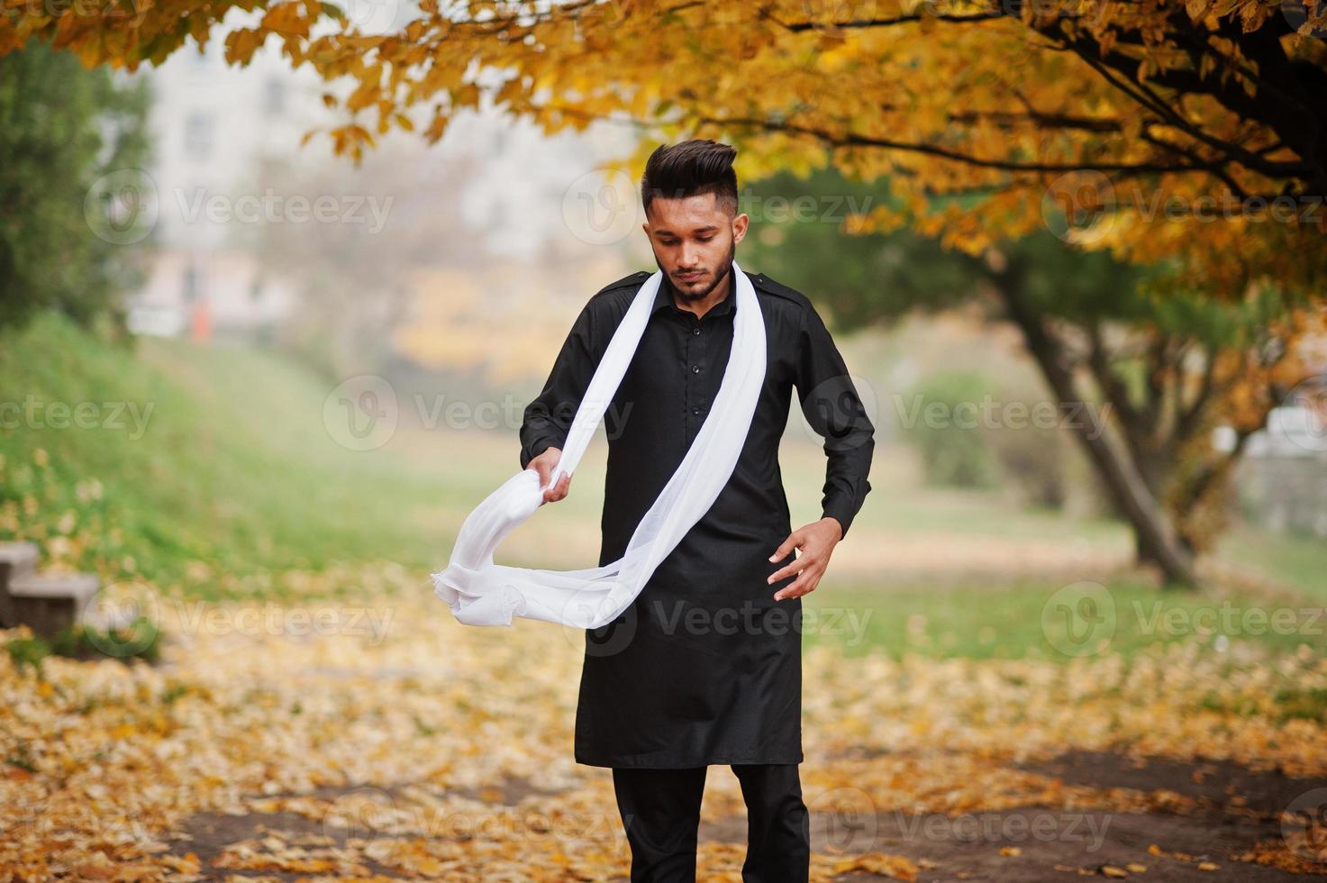 uomo indiano alla moda in abiti tradizionali neri con sciarpa bianca poste all'aperto contro l'albero giallo delle foglie di autunno. foto