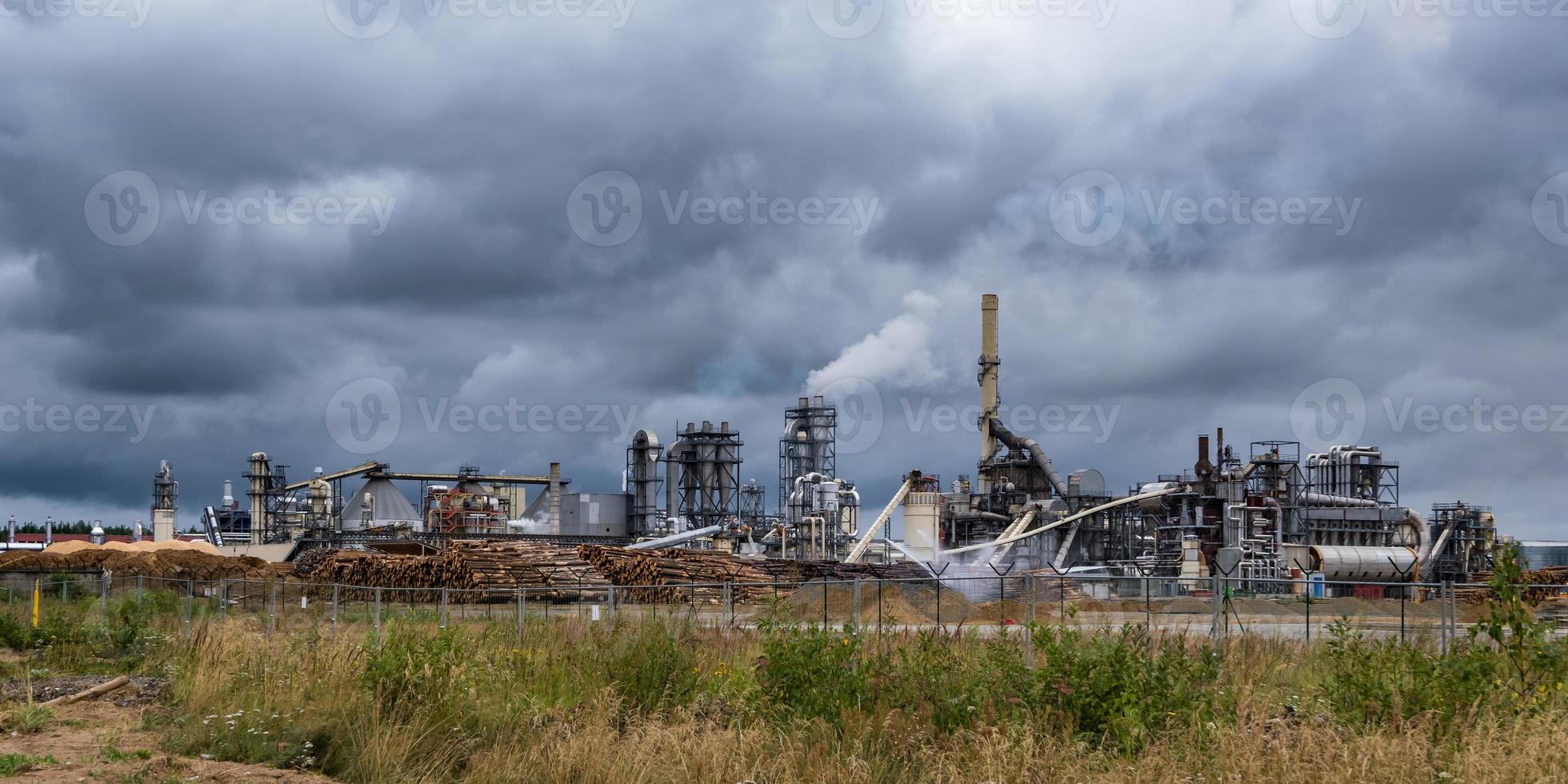 tubi della segheria della pianta di impresa di lavorazione del legno contro un cielo grigio cupo. concetto di inquinamento atmosferico. panorama del paesaggio industriale inquinamento ambientale rifiuti di centrale termica foto