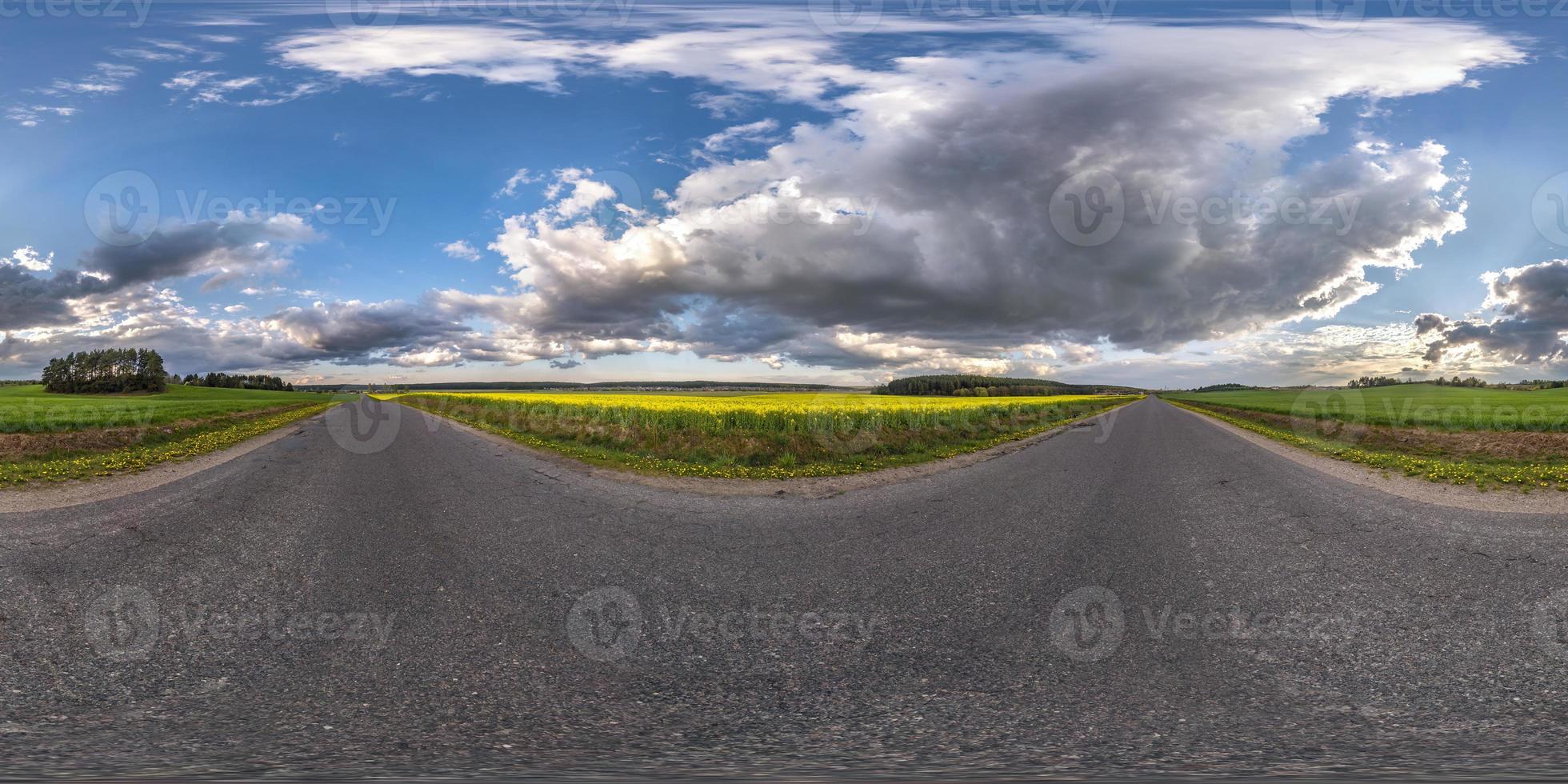 panorama sferico completo senza soluzione di continuità vista angolare a 360 gradi sulla vecchia strada asfaltata senza traffico tra campi con cielo nuvoloso in proiezione equirettangolare, contenuto vr ar foto