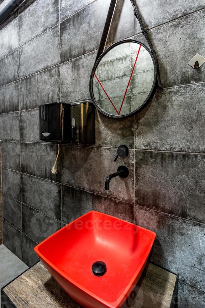 lavabo rosso con rubinetto in un costoso bagno a soppalco in un bar sportivo d'élite su sfondo nero muro di mattoni foto