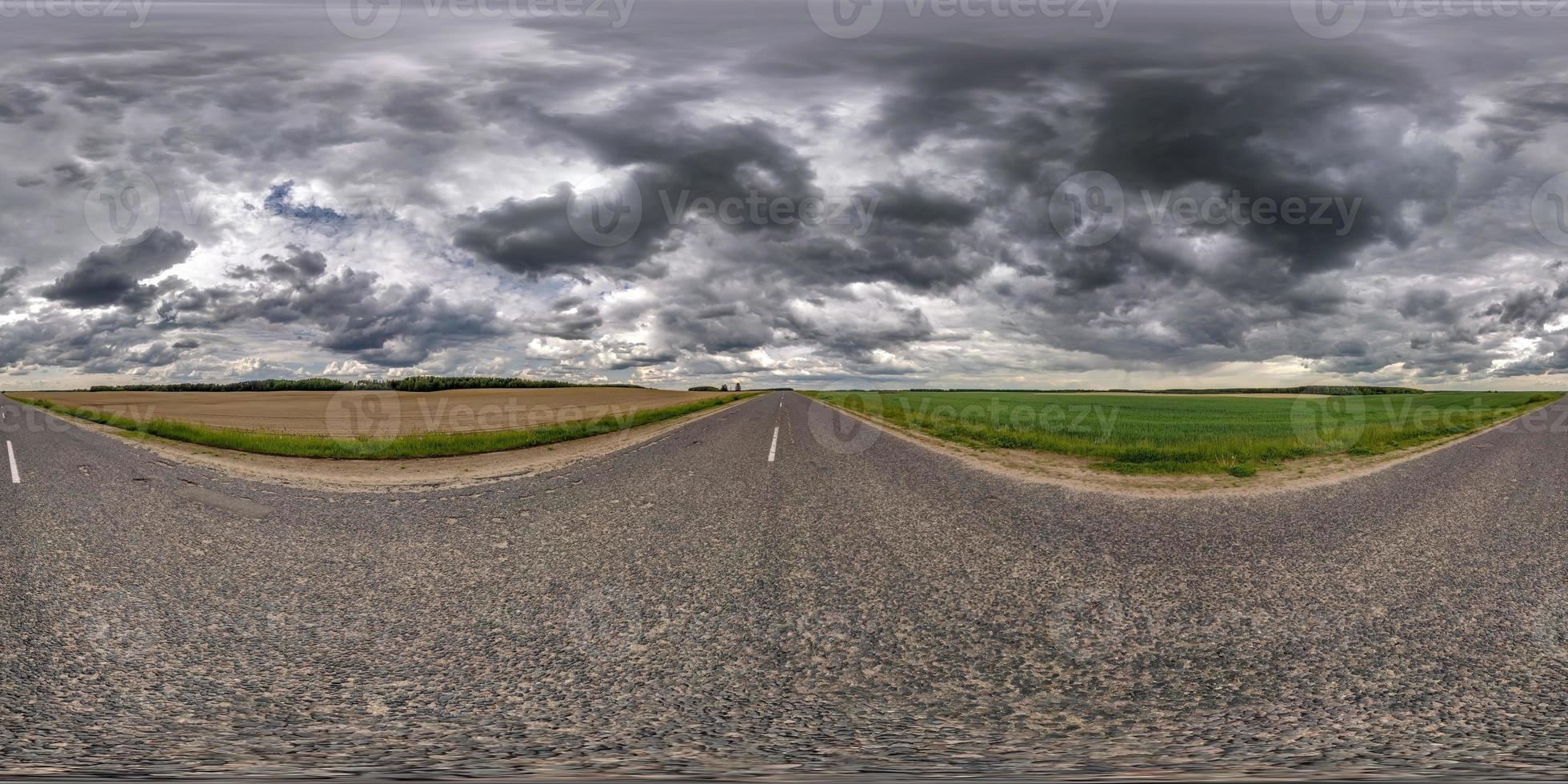 panorama hdr sferico completo senza soluzione di continuità vista angolare a 360 gradi sulla vecchia strada asfaltata senza traffico tra i campi con nuvole nere di pioggia prima della tempesta in proiezione equirettangolare, contenuto di realtà virtuale vr ar foto