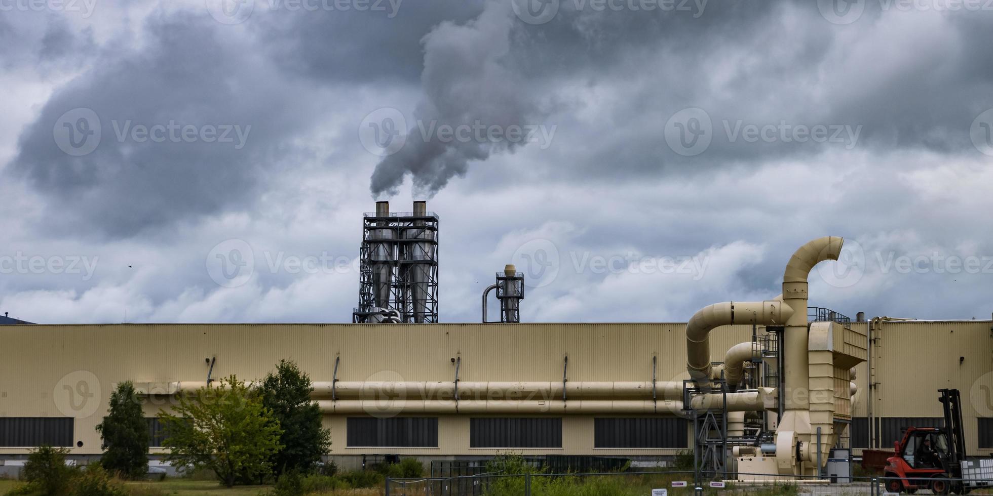 tubi della segheria della pianta di impresa di lavorazione del legno contro un cielo grigio cupo. concetto di inquinamento atmosferico. panorama del paesaggio industriale inquinamento ambientale rifiuti di centrale termica foto