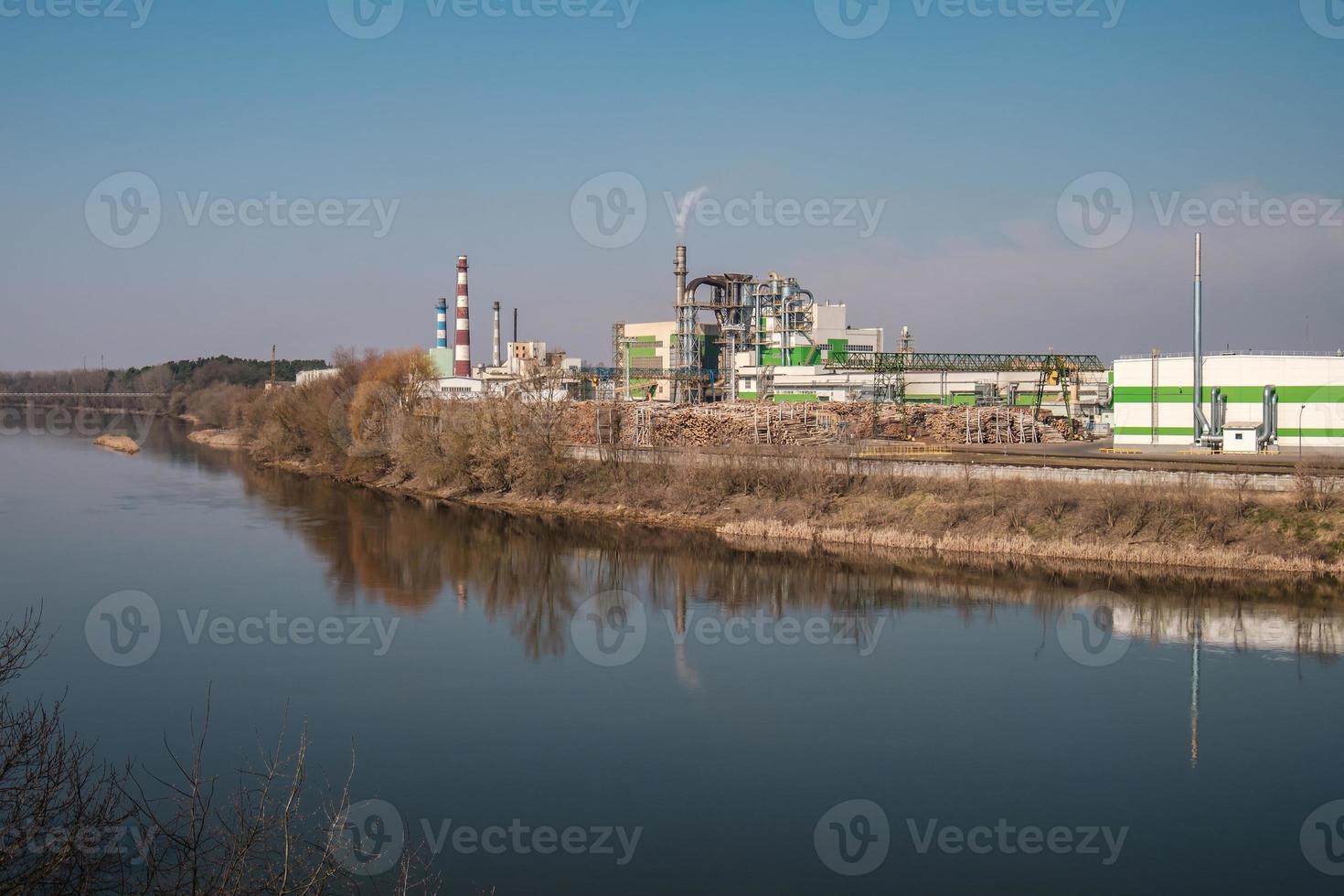 tubi della segheria dell'impianto di impresa di lavorazione del legno vicino al fiume. concetto di inquinamento atmosferico. paesaggio industriale inquinamento ambientale rifiuti di centrale termica foto