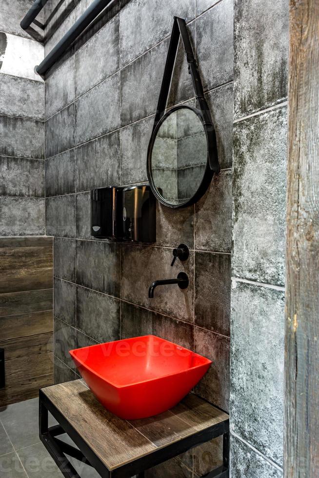 lavabo rosso con rubinetto in un costoso bagno a soppalco in un bar sportivo d'élite su sfondo nero muro di mattoni foto