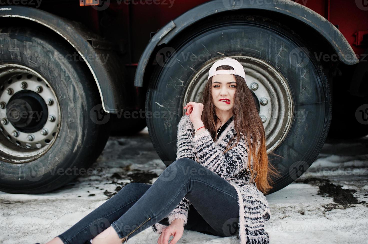 bruna ragazza casual elegante in berretto seduto contro le ruote del camion. foto