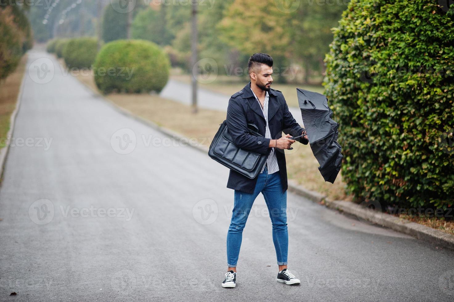 l'uomo alla moda con barba araba alta indossa un cappotto nero con ombrello  e custodia per borsa poste in una giornata di pioggia. 10392701 Stock Photo  su Vecteezy