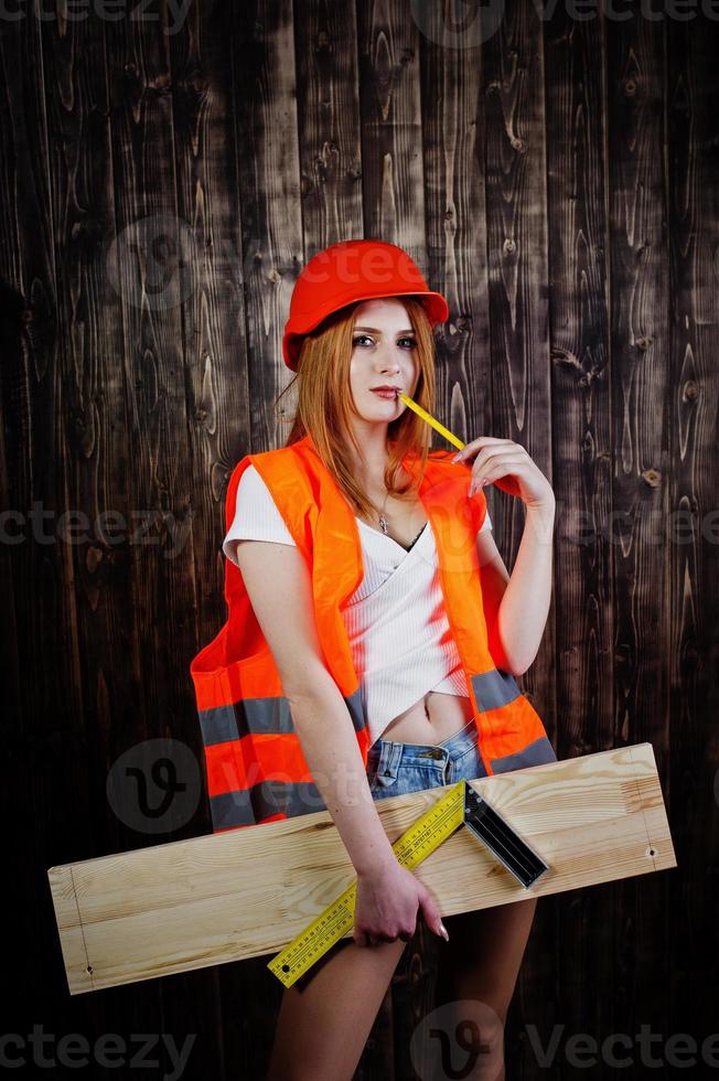 ingegnere donna in arancione protegge il casco e la giacca da costruzione su sfondo di legno che tiene bordo e righello. foto