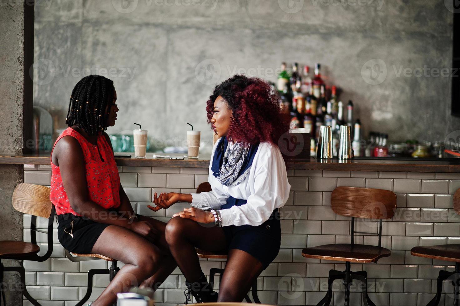 attraenti amiche afroamericane di due ragazze sedute alle sedie contro il bar del pub. foto