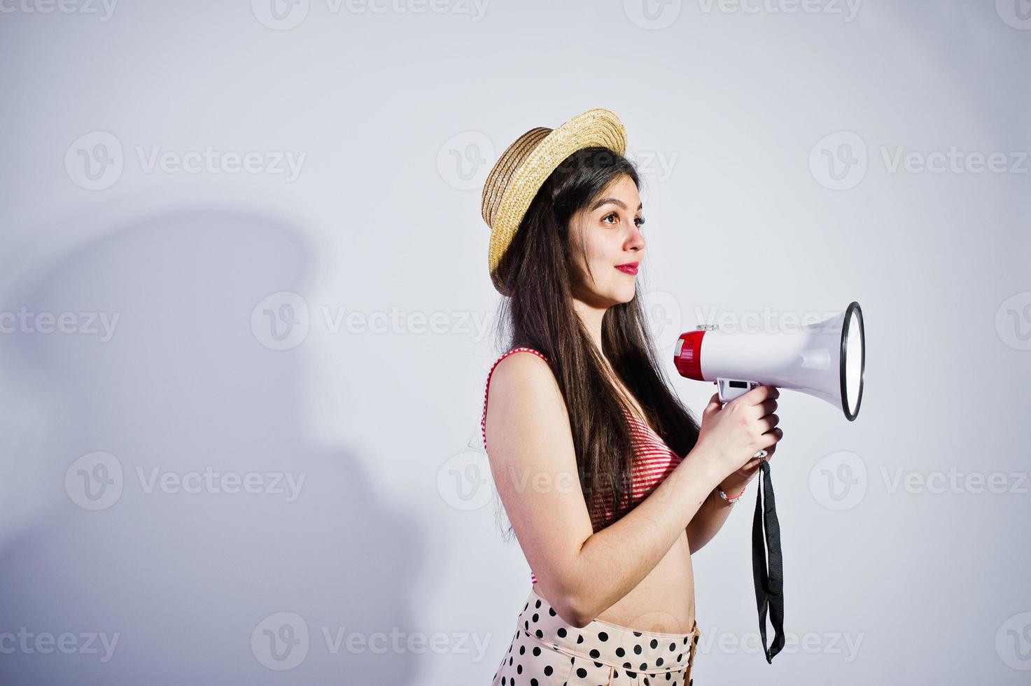 ritratto di una splendida ragazza in costume da bagno e cappello parla nel megafono in studio. foto