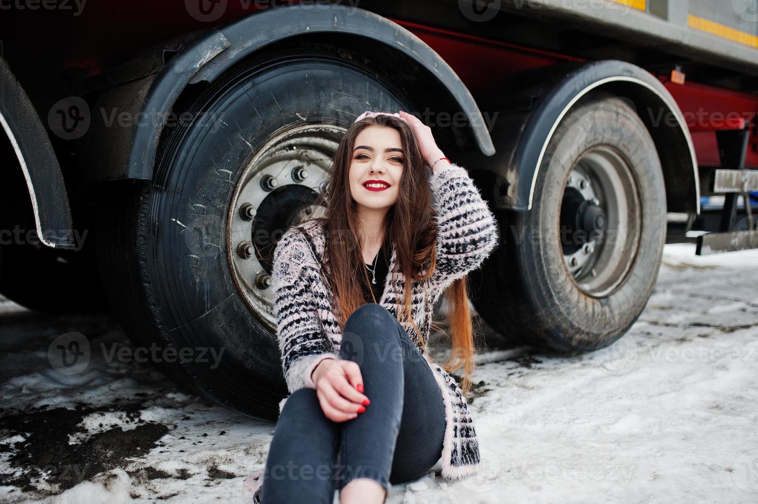 bruna ragazza casual elegante in berretto seduto contro le ruote del camion. foto