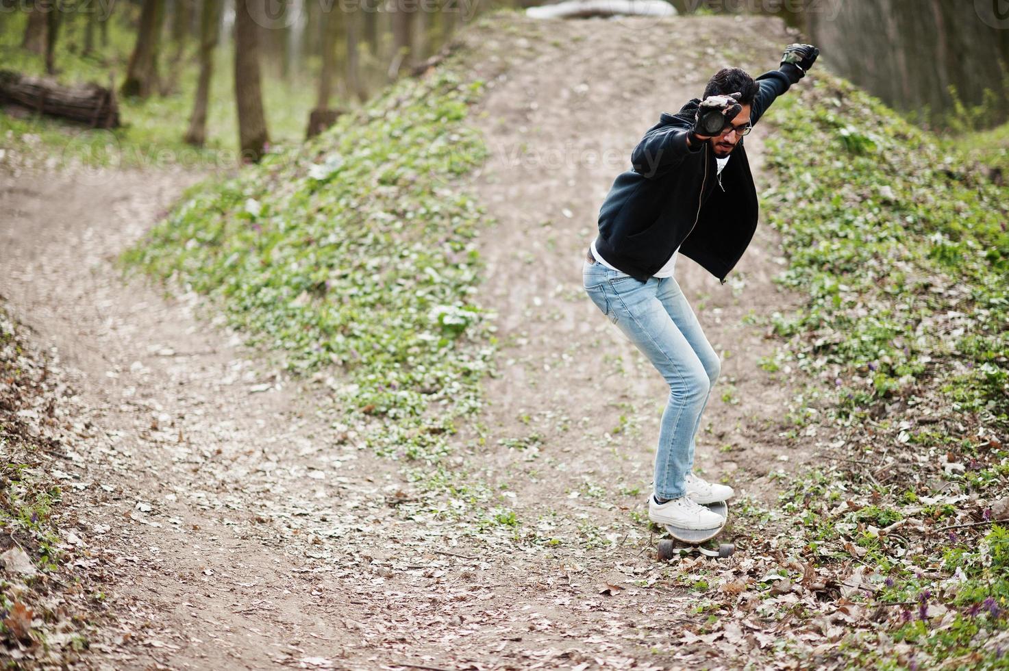 fallire cadendo da uno skateboard. street style uomo arabo in occhiali da vista con longboard su legno. foto