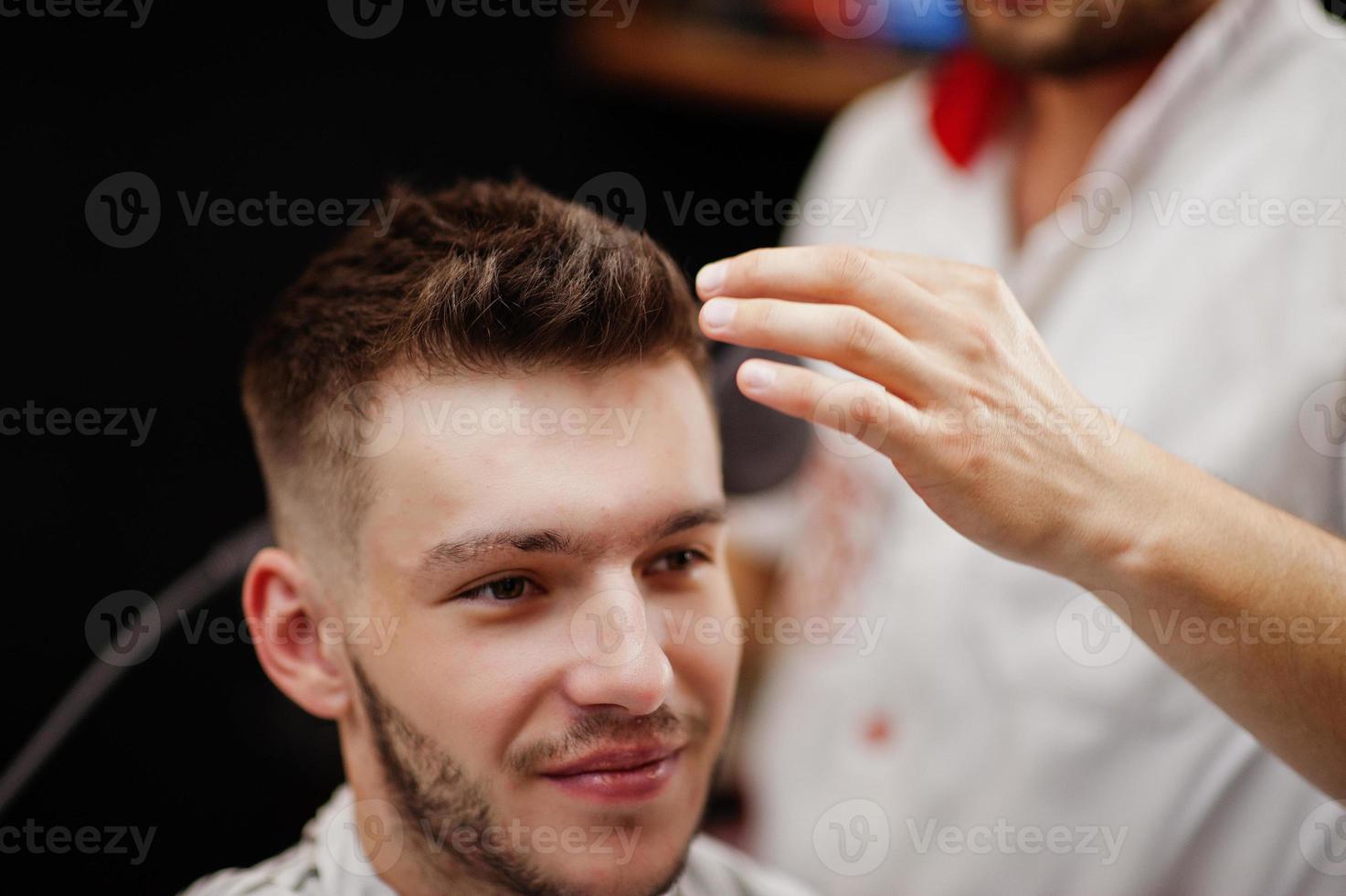 giovane uomo barbuto che si fa tagliare i capelli dal parrucchiere mentre è seduto su una sedia al barbiere. anima da barbiere. foto