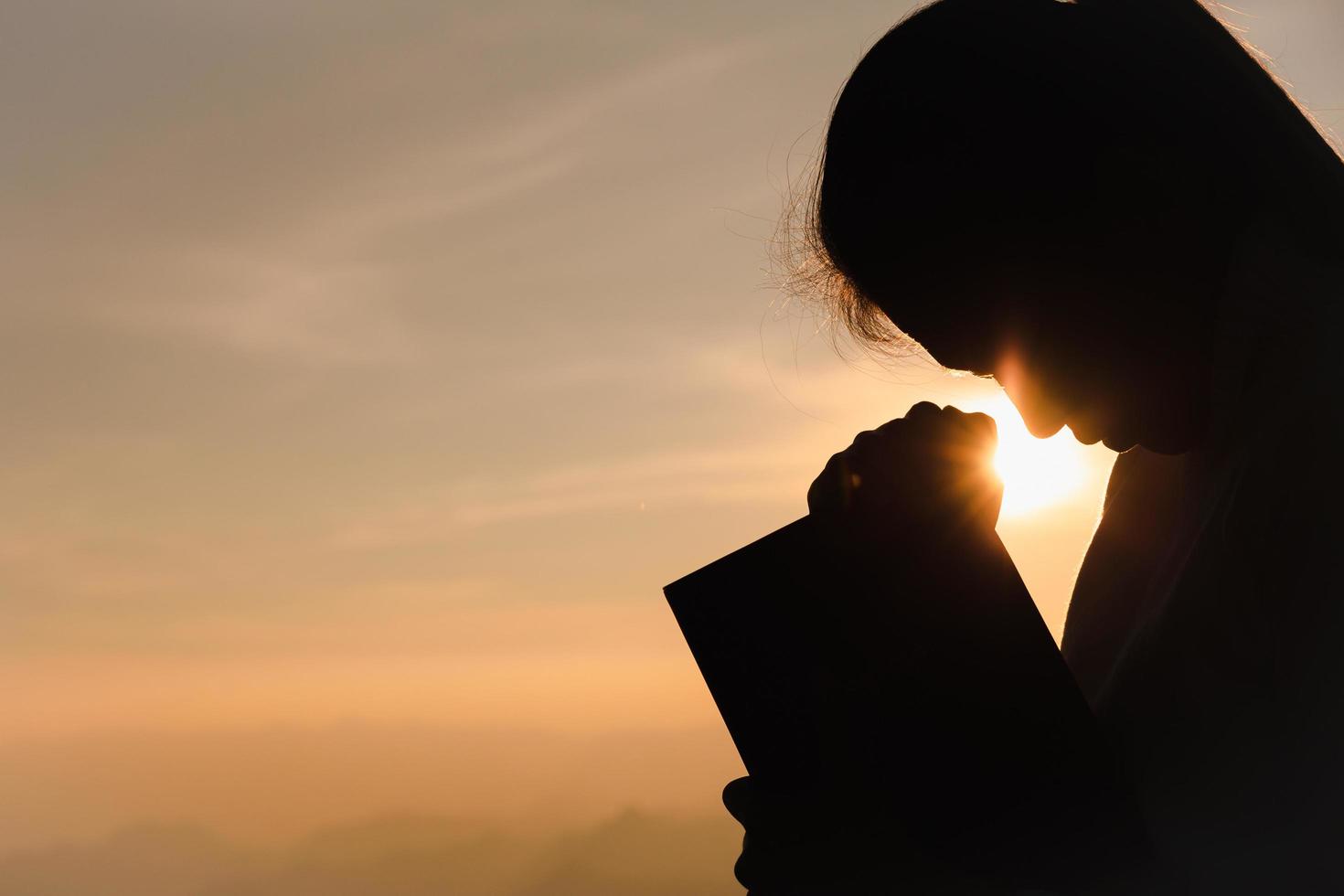 silhouette di giovane donna cristiana che prega con la Sacra Bibbia all'alba, sfondo del concetto di religione cristiana. foto