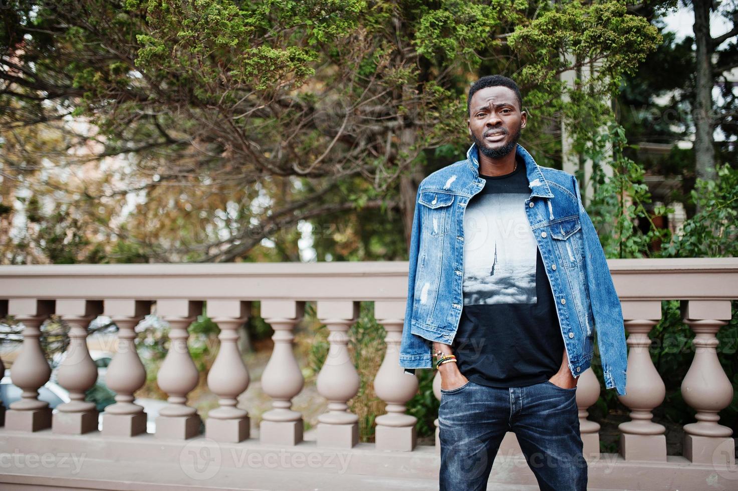 giovane modello attraente uomo afroamericano serio. bel ragazzo moderno in giacca di jeans in piedi sulla strada urbana della città. foto