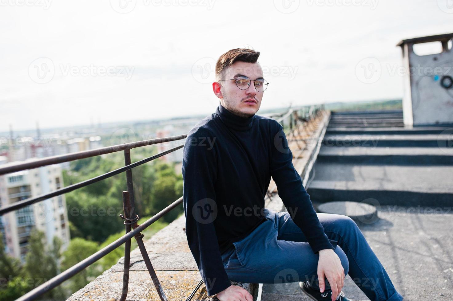 sognatore elegante uomo macho in golf nero e occhiali posati sul tetto. foto