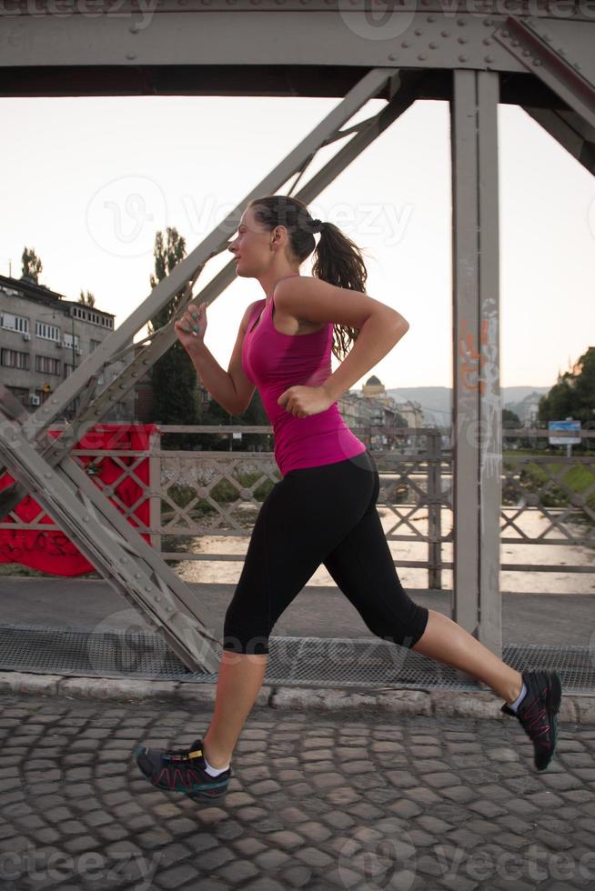 donna che fa jogging attraverso il ponte al mattino soleggiato foto