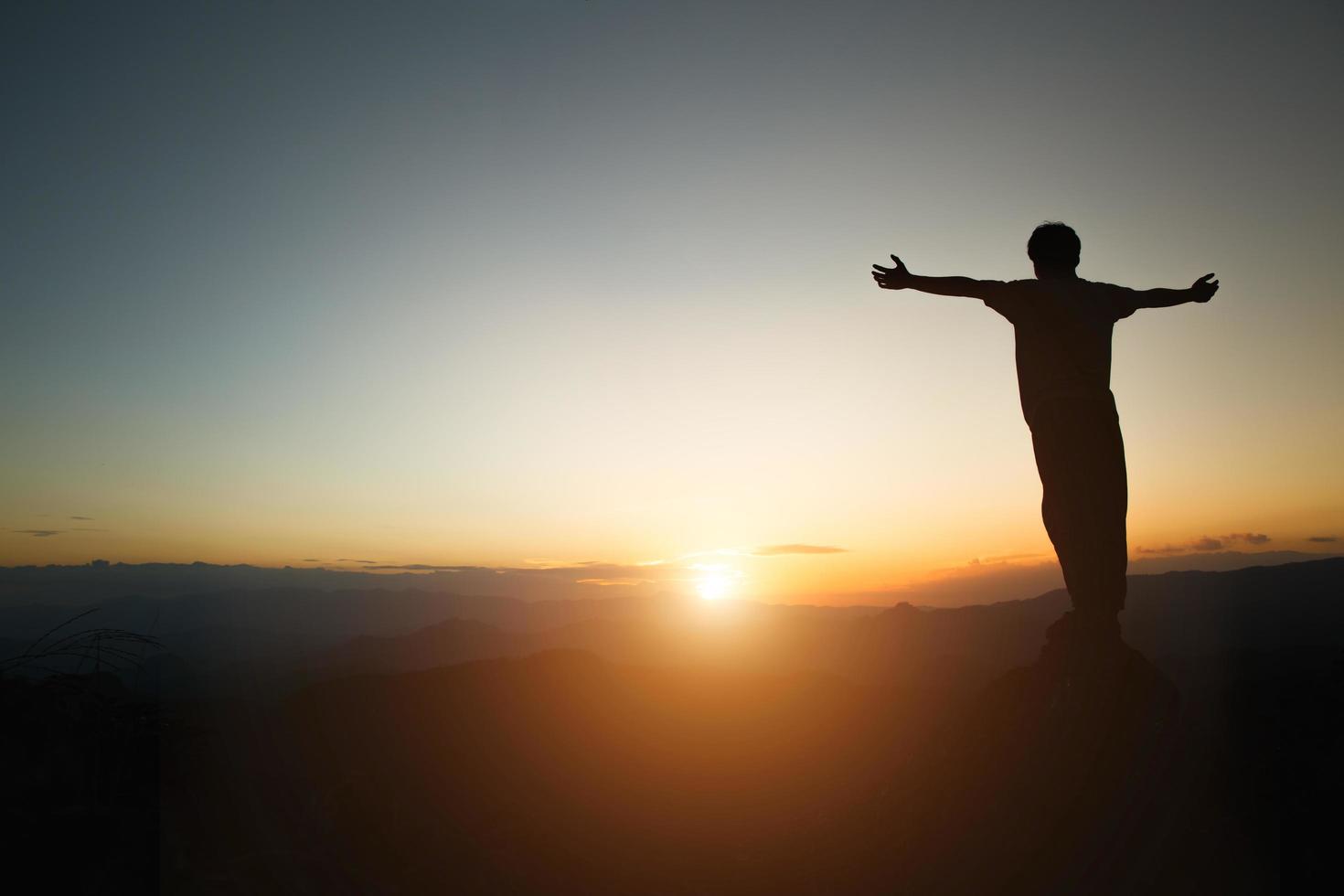 silhouette di uomo alza la mano pregando in cima alla montagna e il cielo al tramonto sfondo astratto. concetto di libertà e avventura di viaggio. foto