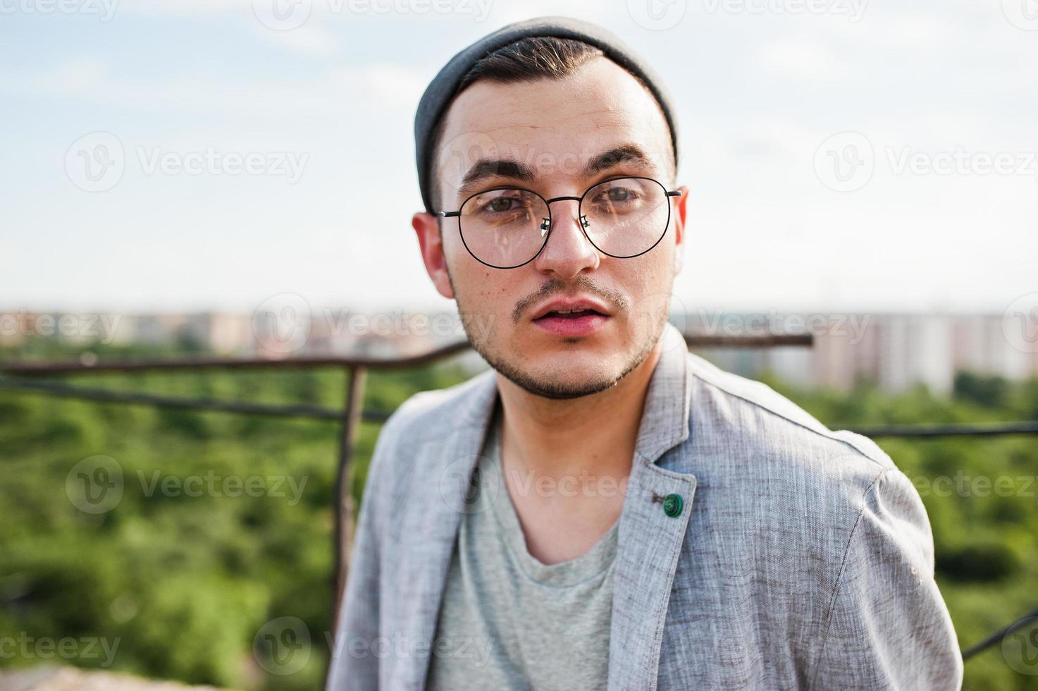 sognatore elegante uomo macho in abito grigio, cappello e occhiali in posa sul tetto. foto