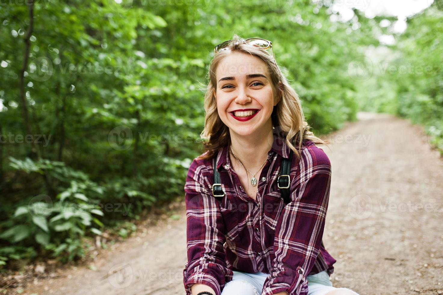 ritratto di una bella ragazza bionda in camicia scozzese seduta per terra in campagna. foto