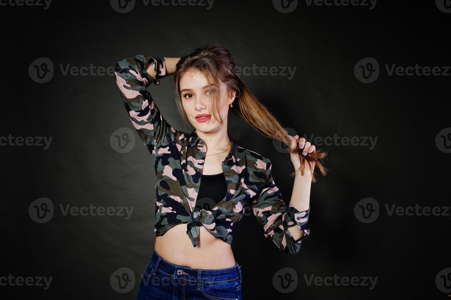 bella ragazza bruna indossare camicia militare e jeans, in posa in studio su sfondo grigio. ritratto del modello in studio. foto