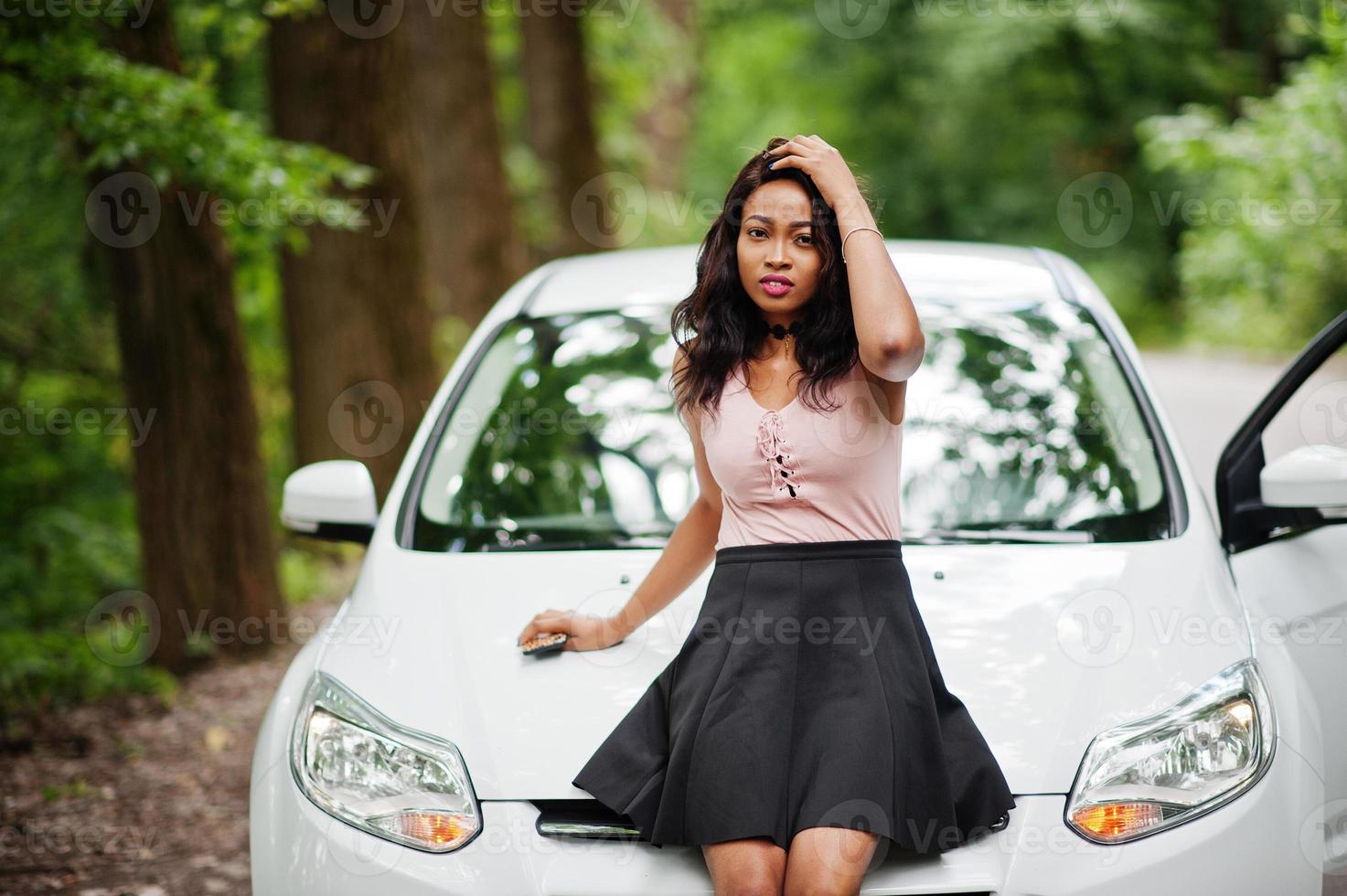 donna afroamericana posata contro un'auto bianca in strada forestale. foto
