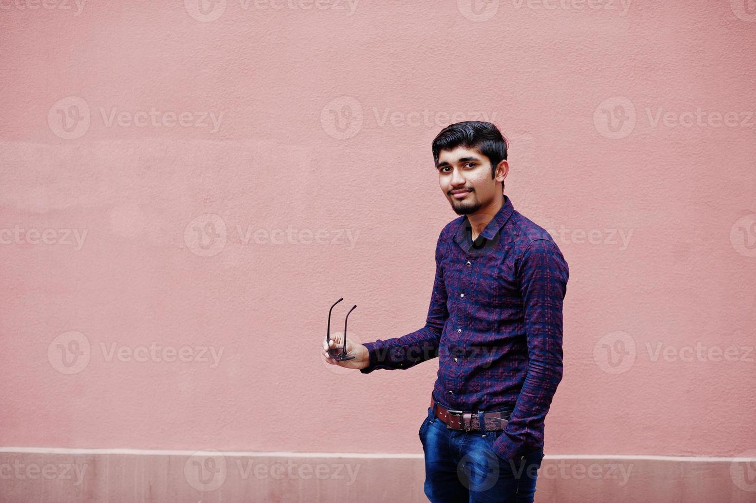 giovane indiano su camicia e occhiali da sole in posa contro il muro rosa. foto